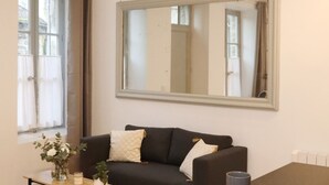 A living room with a black sofa, a wooden coffee table, a mirror, and a window with curtains. - Notre Dame de Senlis par La Boite en plus (Senlis)
