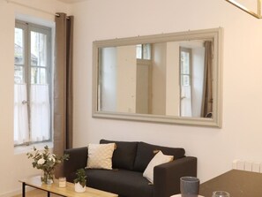 A living room with a black sofa, a wooden coffee table, a mirror, and a window with curtains.