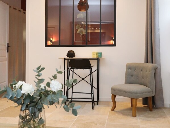 A room with a chair, a small table, a vase with flowers, and a window with a view.