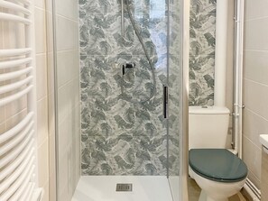 A shower with a glass door, a toilet, and a wall with a leaf pattern.