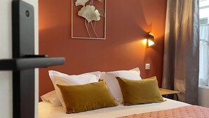 A hotel room with a bed, pillows, a wall-mounted light, and a window with curtains. - Notre Dame de Senlis par La Boite en plus (Senlis)