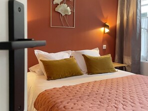 A hotel room with a bed, pillows, a wall-mounted light, and a window with curtains.