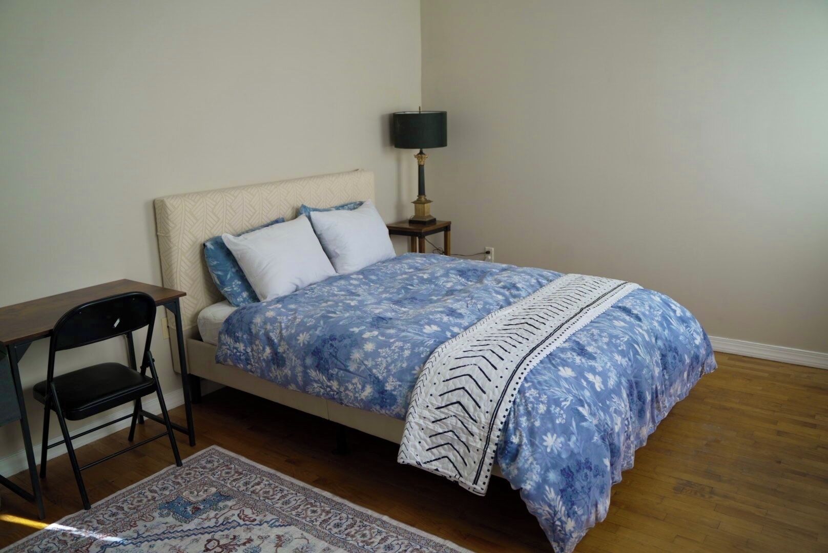 A bedroom with a bed, a desk, a chair, a lamp, and a rug.