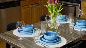 A kitchen with wooden cabinets, a microwave, and a stove. There is a dining table set with blue plates and glasses.