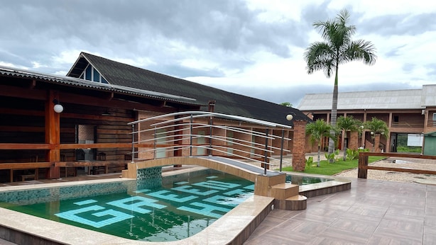 A swimming pool with a wooden deck and a bridge, surrounded by buildings with a rustic design. - Hotel Villa Green  (Tome-Acu)