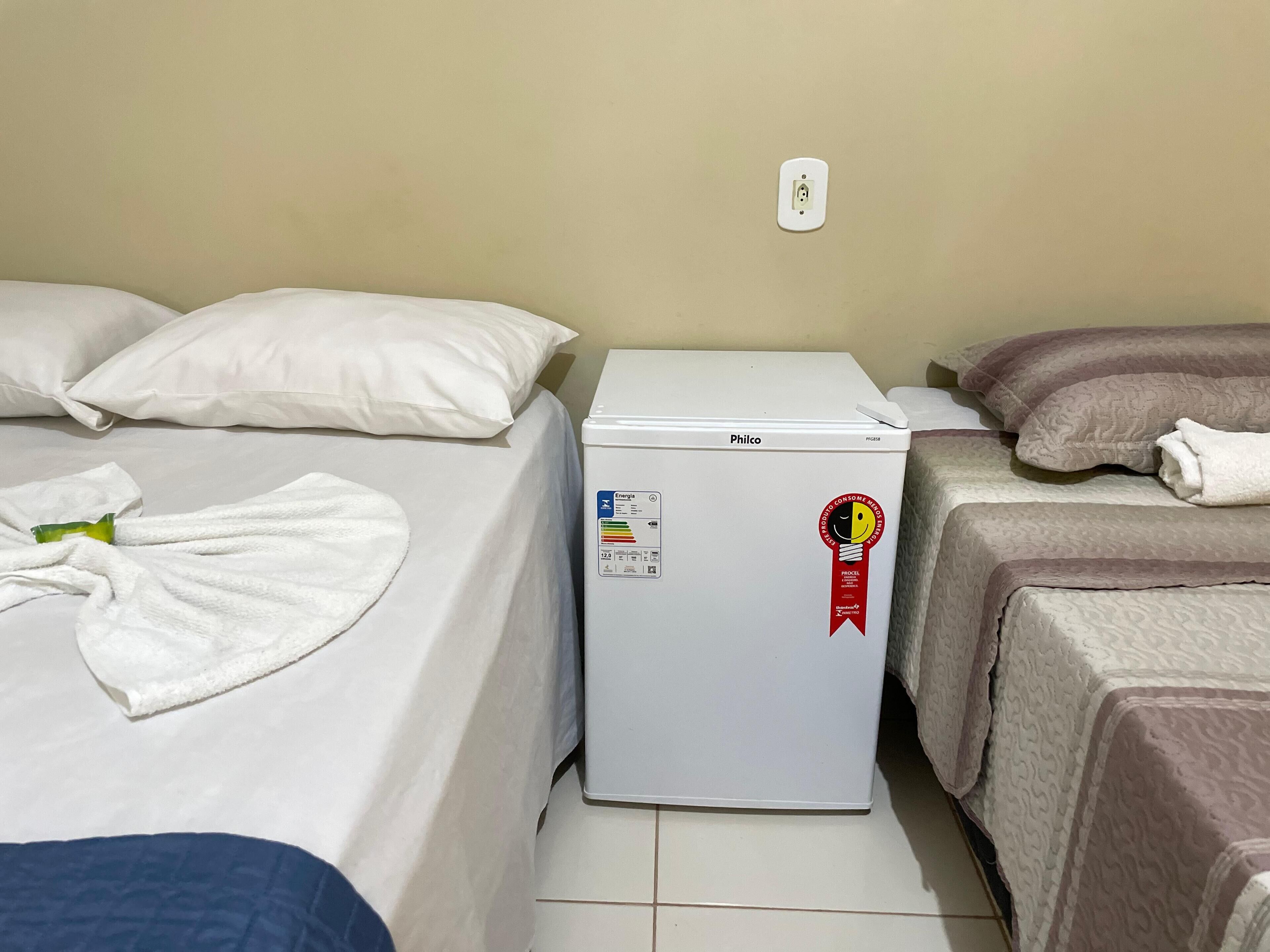 A hotel room with two beds, a white refrigerator, and a power outlet on the wall.