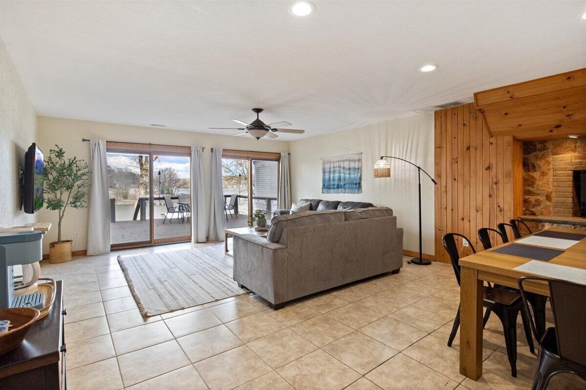 A spacious living area with a sofa, dining table, and chairs. There is a ceiling fan, a television, and a fireplace.