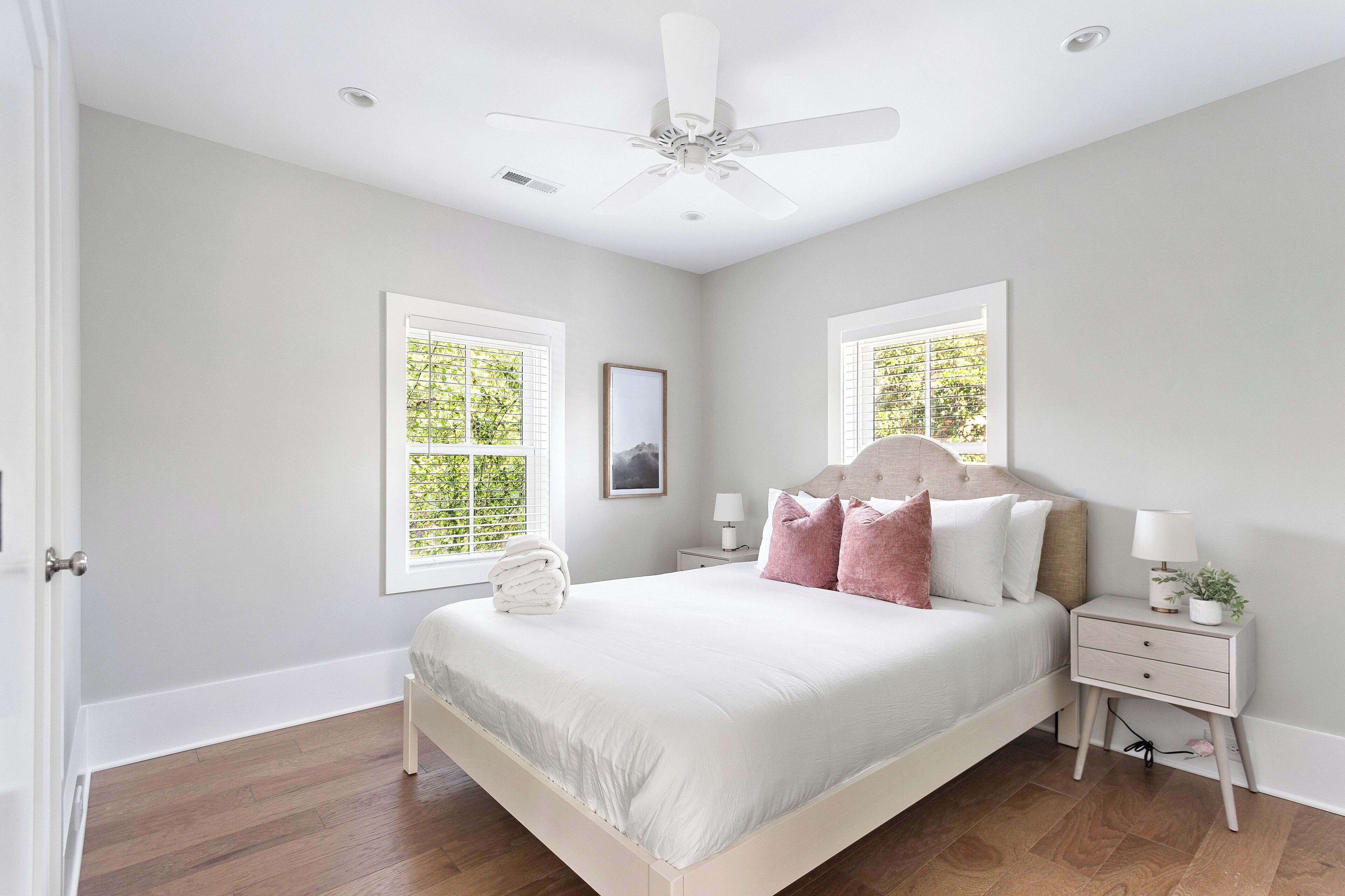 Une chambre à coucher avec un lit, des tables de chevet, un ventilateur de plafond et des fenêtres.