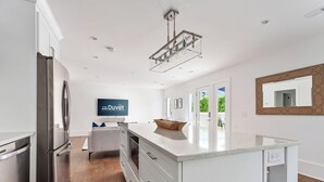 Una cocina moderna con un refrigerador de acero inoxidable, una isla grande con encimera de mármol y una lámpara colgante.