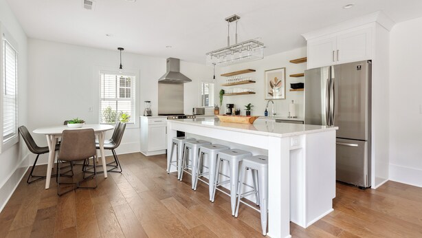 Una cocina moderna con armarios blancos, un refrigerador de acero inoxidable y una barra con taburetes.