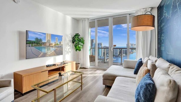 Ein modernes Wohnzimmer mit großem Fenster, Flachbildfernseher, einer Couch, einem Couchtisch und einer Pflanze.