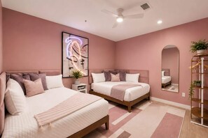 Un dormitorio con dos camas, un ventilador de techo, un espejo grande y una planta.
