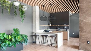 A modern kitchen with a central island, bar stools, hanging plants, and pendant lighting.