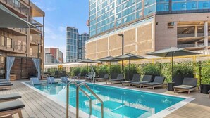 A rooftop pool with lounge chairs and umbrellas, surrounded by buildings.