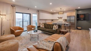 A modern living room with a sofa, chairs, a coffee table, and a dining area with a kitchen in the background.