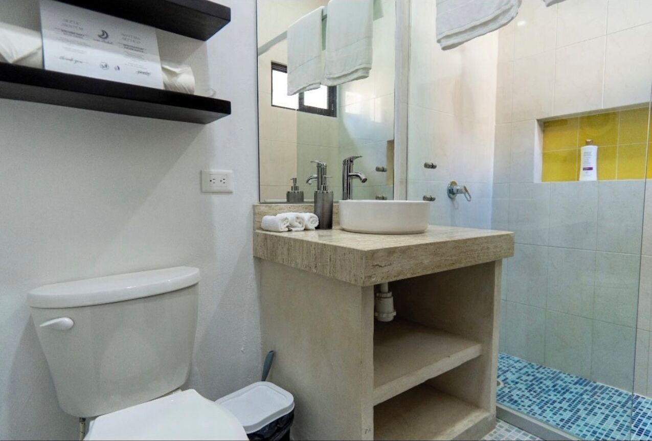 Ein Badezimmer mit Toilette, Waschbecken, Spiegel und Duschbereich.