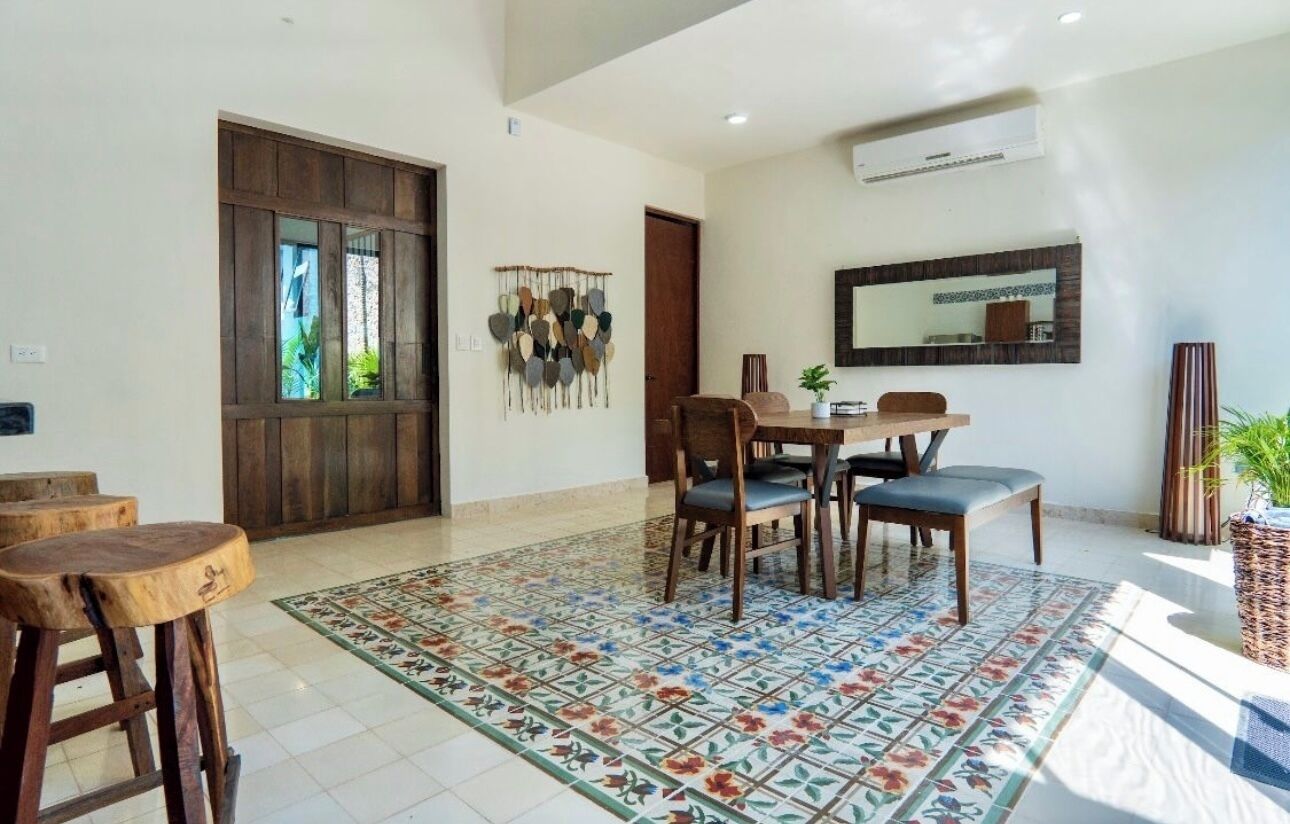 Un coin repas avec une table et des chaises en bois, un tapis à motifs et un grand miroir au mur.