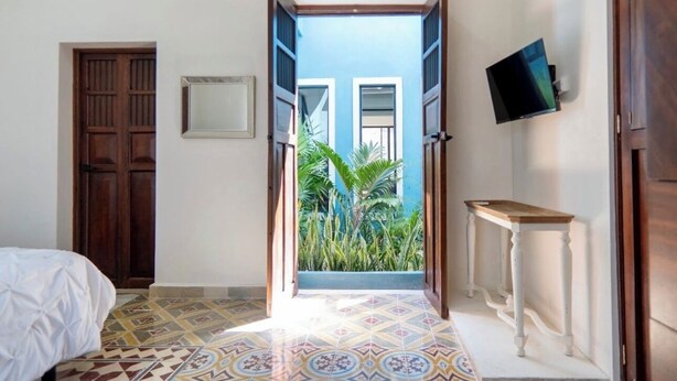 Une chambre à coucher avec un lit, un téléviseur fixé au mur et une vue sur un immeuble bleu, visible à travers une porte ouverte.