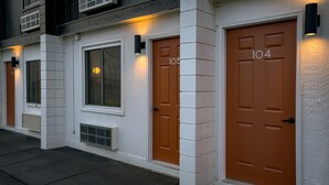 Eine Reihe von Türen mit den Nummern 105 und 104, weiße Backsteinwände und ein kleines Fenster mit einem Kreuz an der Tür.