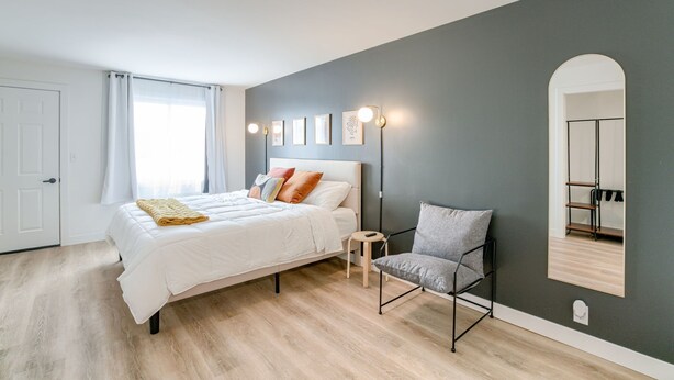 Ein Schlafzimmer mit Bett, Stuhl, Nachttisch, Spiegel und Wandleuchten.