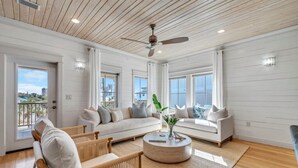 A spacious living room with a high ceiling, large windows, and a ceiling fan.
