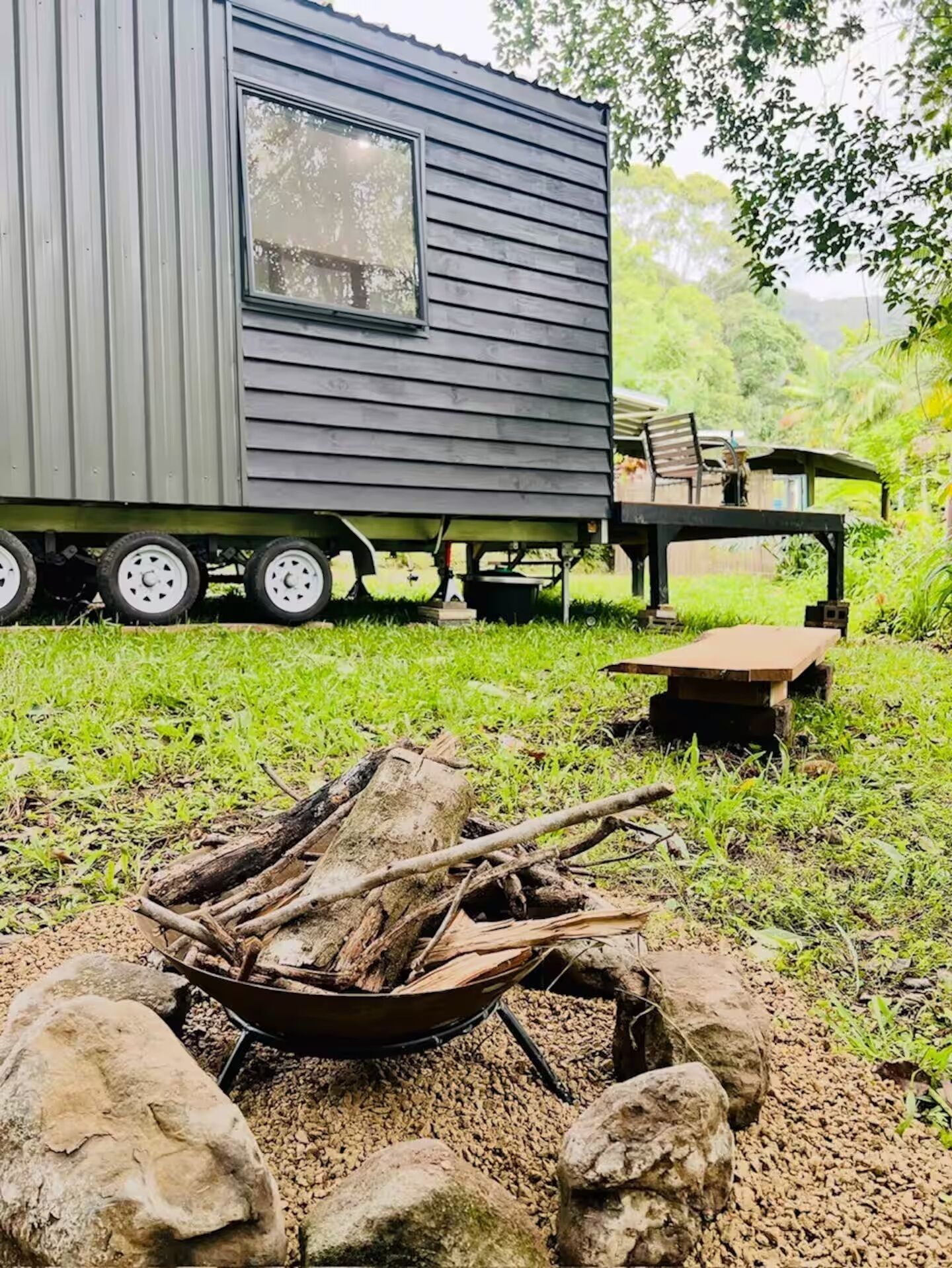Une petite cabane dotée d’une terrasse, d’un foyer extérieur et d’une remorque attelée.