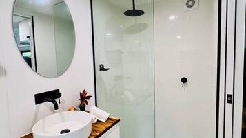 Ein modernes Badezimmer mit einem weißen Waschbecken, Spiegel und einer Duschkabine aus Glas.