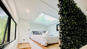 Une chambre moderne avec une lucarne, un lit recouvert de linge de lit blanc et un mur décoratif vert.