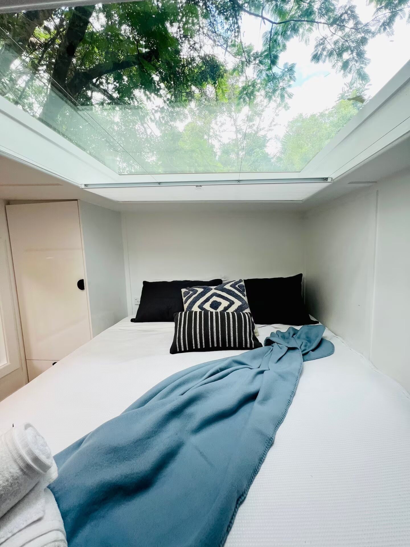 Una habitación con tragaluces, una cama con ropa de cama blanca, almohadas negras y blancas, y una colcha azul.
