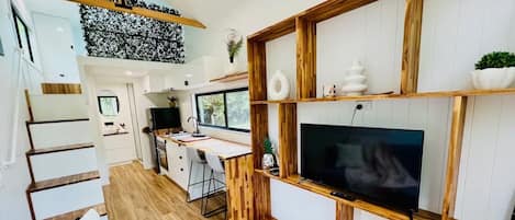 A modern kitchen with a wooden countertop, a built-in TV, and a dining area with a wooden table and chairs.