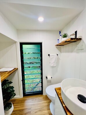 Une petite salle de bain comprenant des toilettes, un lavabo, un porte-serviettes et une fenêtre avec un store à motifs verts.