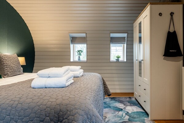 A bedroom with a bed, two windows, a wardrobe, and a hanging bag. - Stunning One Bedroom Eco-Retreat in Old Chalford (Chipping Norton)
