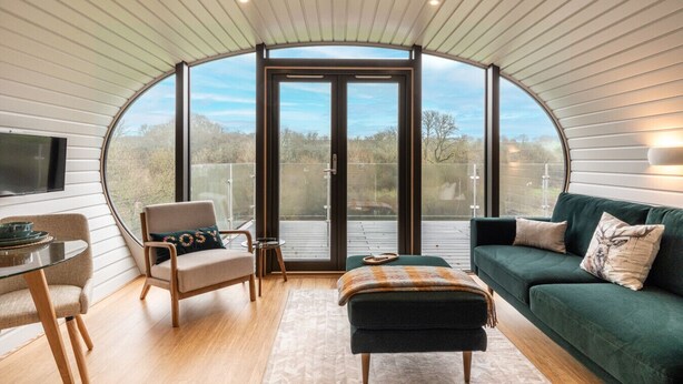 Un interior moderno con techo curvo, una zona de estar con sofá y sillón, una mesita y un ventanal grande que ofrece vistas al exterior.