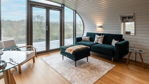 Una sala de estar moderna con una mesa de comedor de vidrio, un sofá verde y un amplio ventanal corredero que da a una terraza exterior.