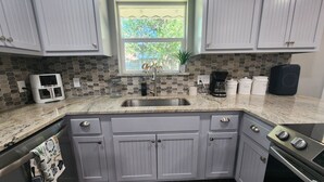 A kitchen with grey cabinets, a granite countertop, a coffee maker, and a window with a view of greenery. - Spacious 4-bdr house in charming Del City with AC, WiFi and 9 min of Tinker AFB (Del City)