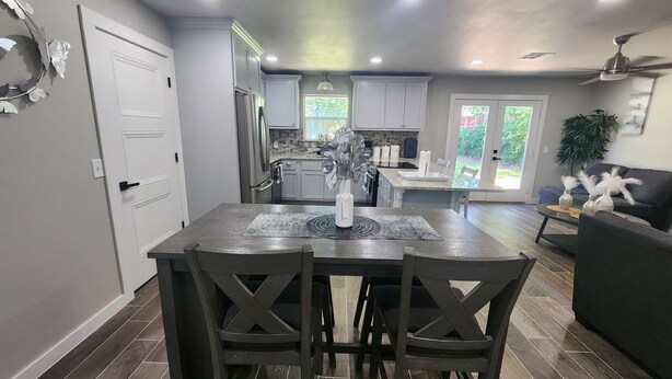 A modern kitchen with white cabinets, a dining table with dark chairs, and a ceiling fan. - Spacious 4-bdr house in charming Del City with AC, WiFi and 9 min of Tinker AFB (Del City)
