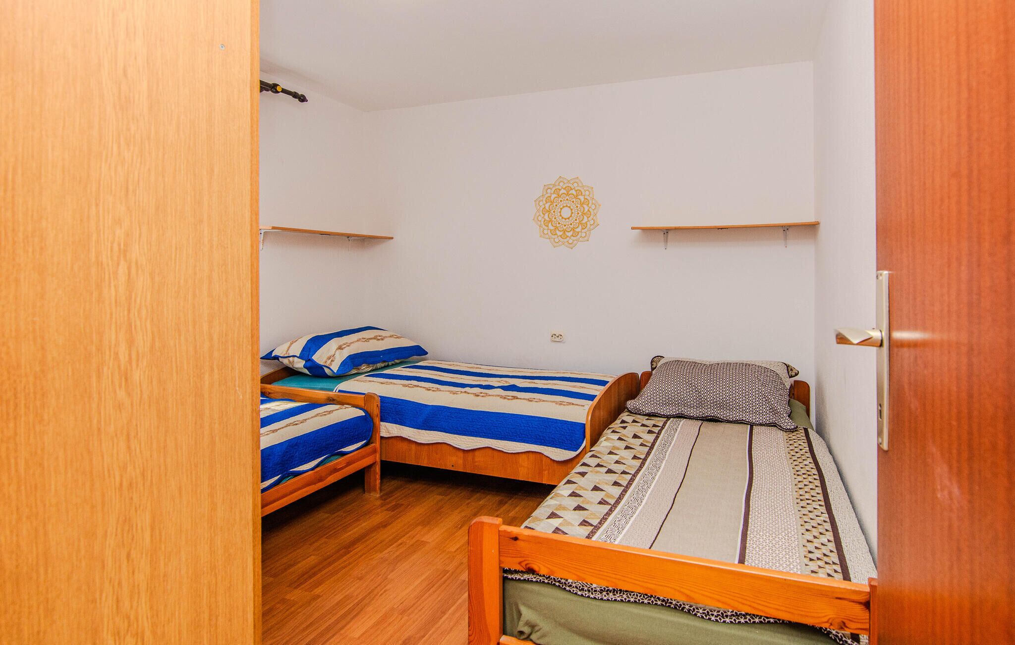 Pequeña habitación compacta con dos literas de madera, una puerta de madera y una pared blanca con un mandala dorado decorativo.