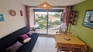 A cozy room with a sofa, a table, a fan, and a view of the neighborhood. - Two-room flat, Le Grau du Roi (Le Grau-du-Roi)