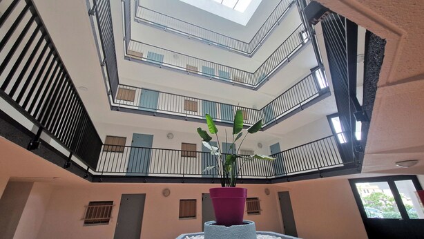 A multi-level atrium with a central potted plant, balconies with railings, and a high ceiling with skylights. - Two-room flat, Le Grau du Roi (Le Grau-du-Roi)