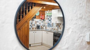 Eine Küche mit weißen Schränken, einer Holztreppe, einer gefliesten Rückwand und einer Uhr an der Wand.