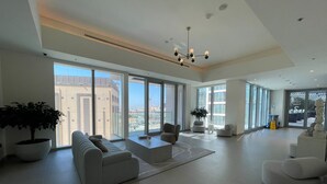 Ein geräumiger Wohnbereich mit einer Sofagarnitur, einem Couchtisch und einer Chandelüster. Große Fenster bieten Blick auf die Stadt.