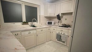 Une cuisine avec des meubles blancs, un four à micro-ondes, un four traditionnel et un réfrigérateur.