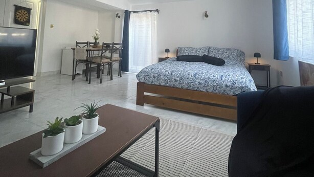 Une chambre moderne avec un grand lit, une télévision, un coin repas et une petite cuisine.