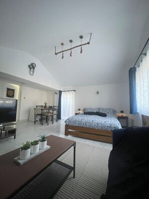 Ein modernes Schlafzimmer mit einem großen Bett, einem Fernseher, einem Essbereich und einer kleinen Küche.
