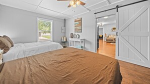 Een slaapkamer met een bed, een plafondventilator, een schuifdeur, een raam en uitzicht op de omgeving.