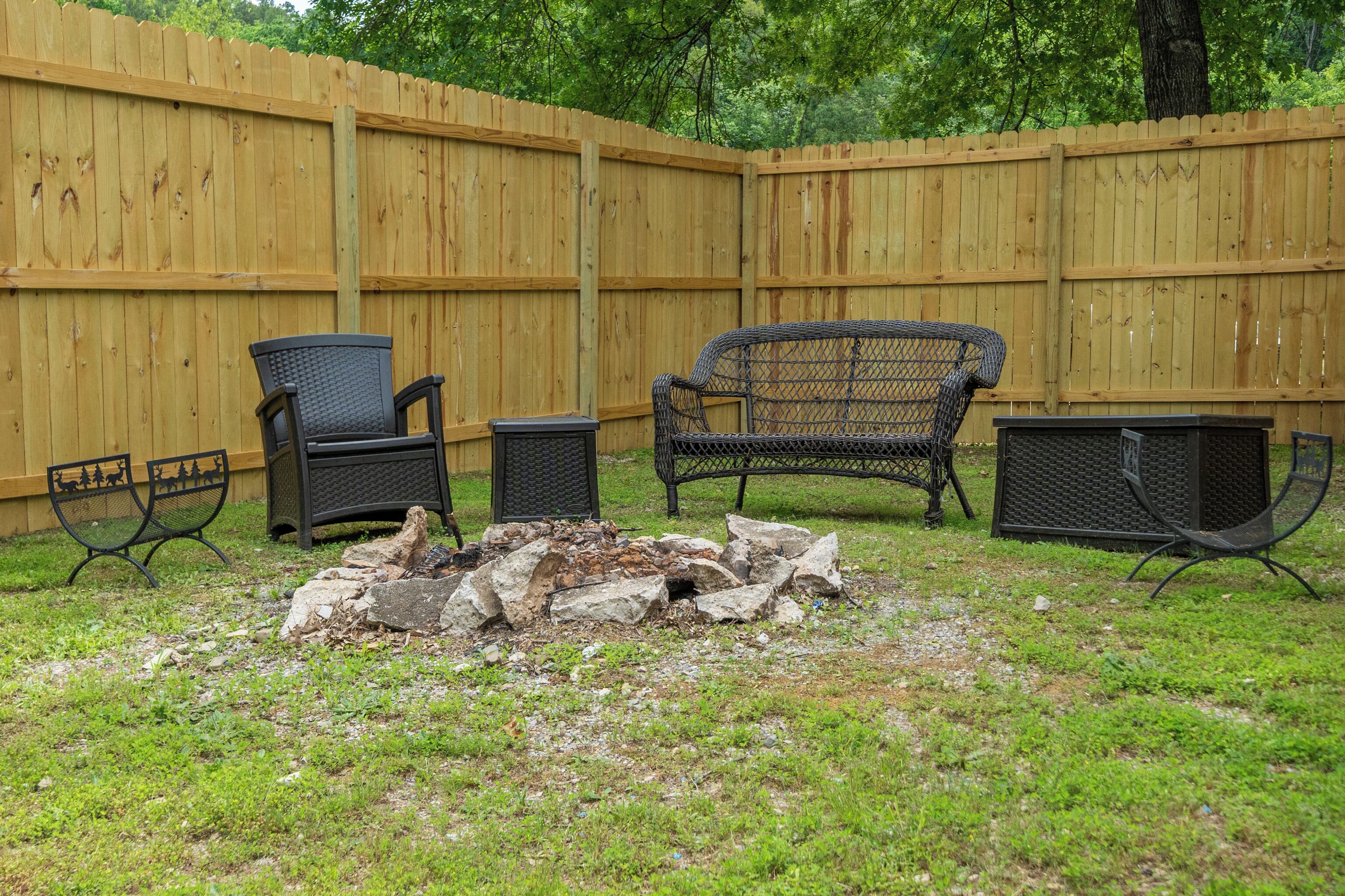 A backyard with a wooden fence, a fire pit, and outdoor furniture including two chairs and a table.