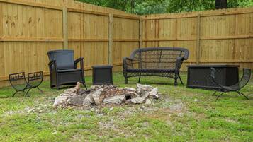 A backyard with a wooden fence, a fire pit, and outdoor furniture including two chairs and a table.