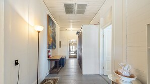 A hallway with a wooden floor, a bench, a painting, and a small table with a decorative item. - The Downtown Historic Island Hotel Room 27 (Cedar Key)