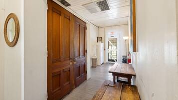 A hallway with wooden doors, a bench, and a white wall with a framed picture.