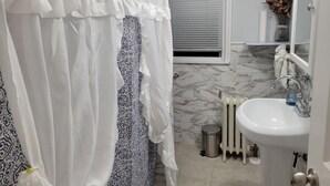 Een badkamer met een wit wastafel, een radiator, een prullenbak en een raam met zonwering.